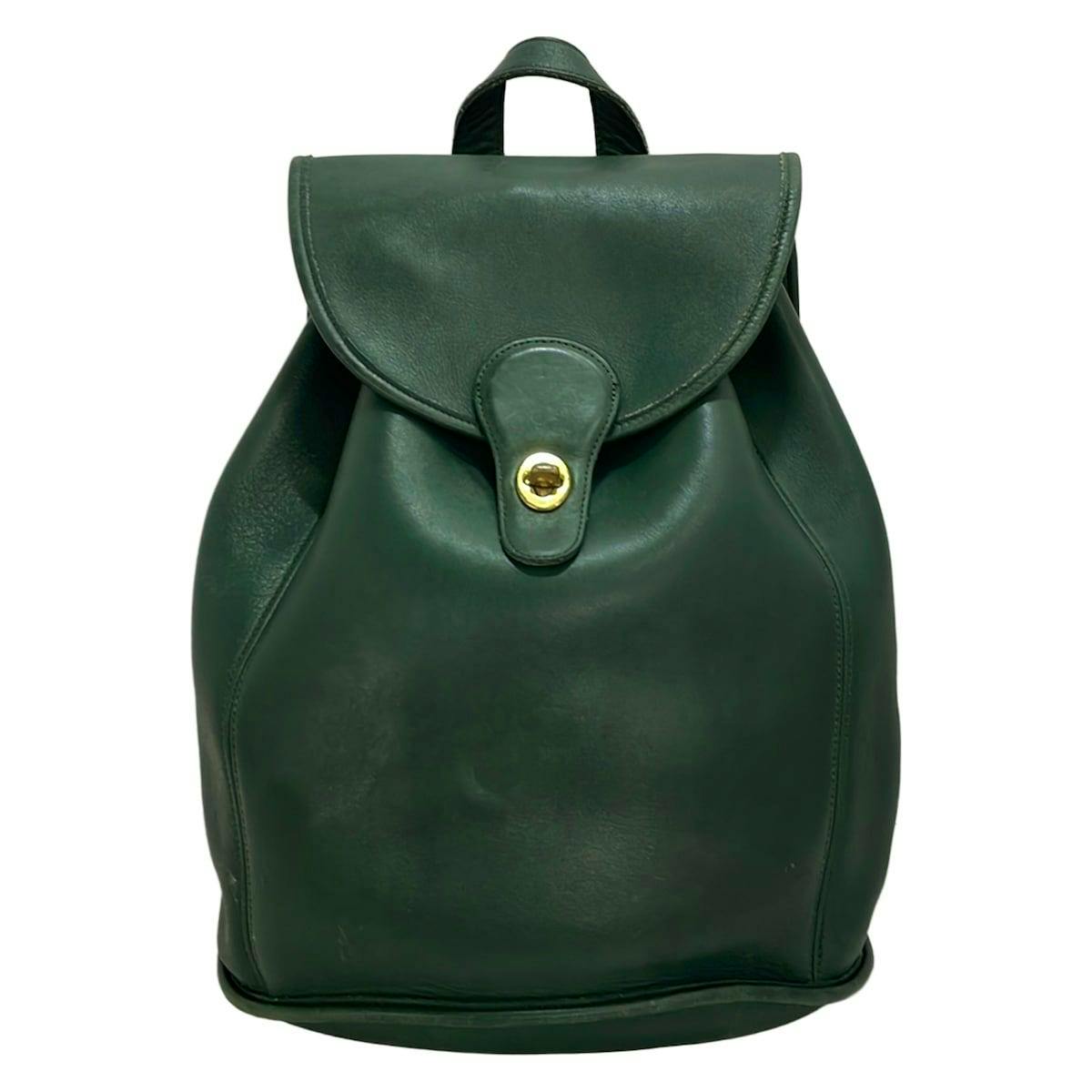 Front view of a dark green Coach leather backpack with a flap and gold turn-lock closure.