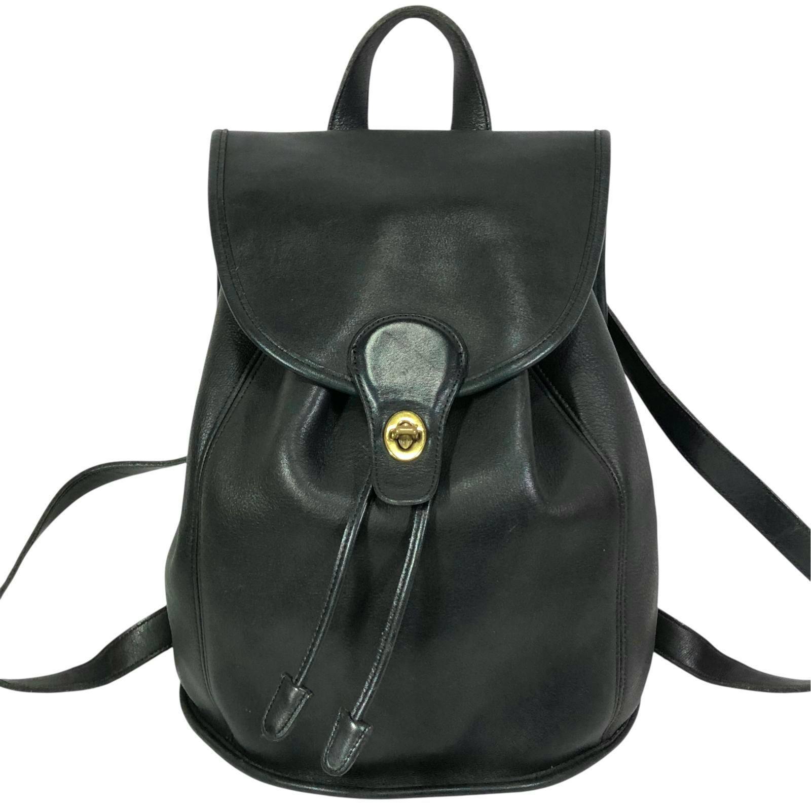 Front view of a black leather Coach backpack with flap, drawstring, and gold turn-lock closure.