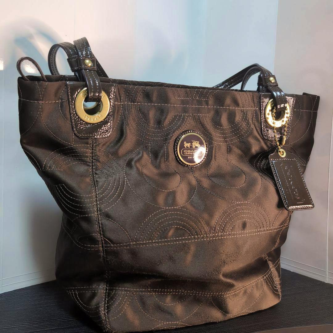 Front view of a Coach Alex quilted op-art canvas tote bag with circular stitched pattern, gold hardware, and a leather hang tag.