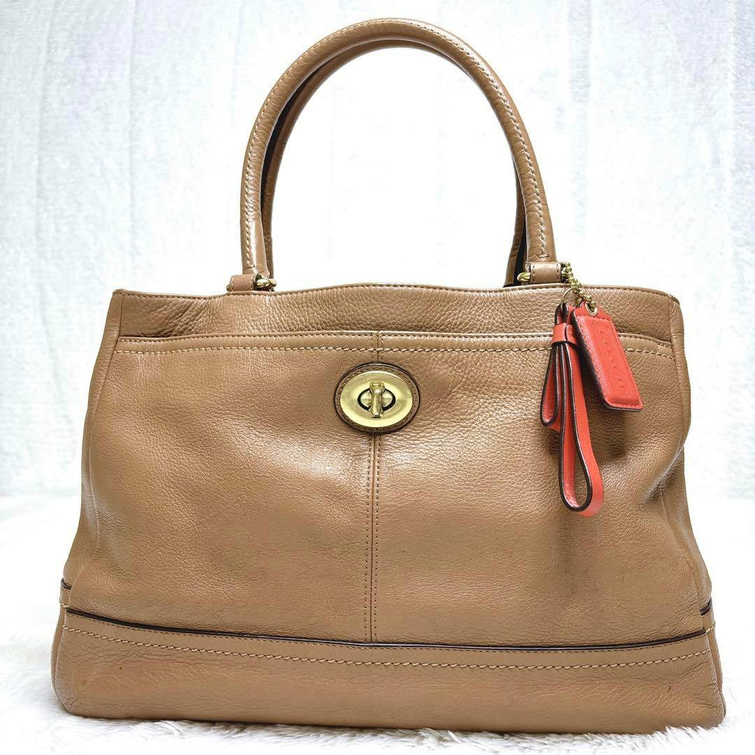 Camel-colored leather Coach tote bag with top handles and a red Coach hangtag, front view.