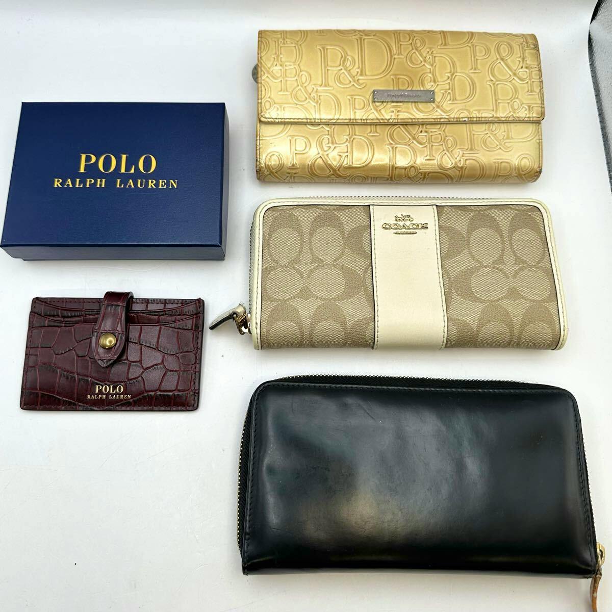 A flat lay photo of several wallets and a POLO Ralph Lauren box arranged on a white background, including a Coach zip-around and a black leather wallet.