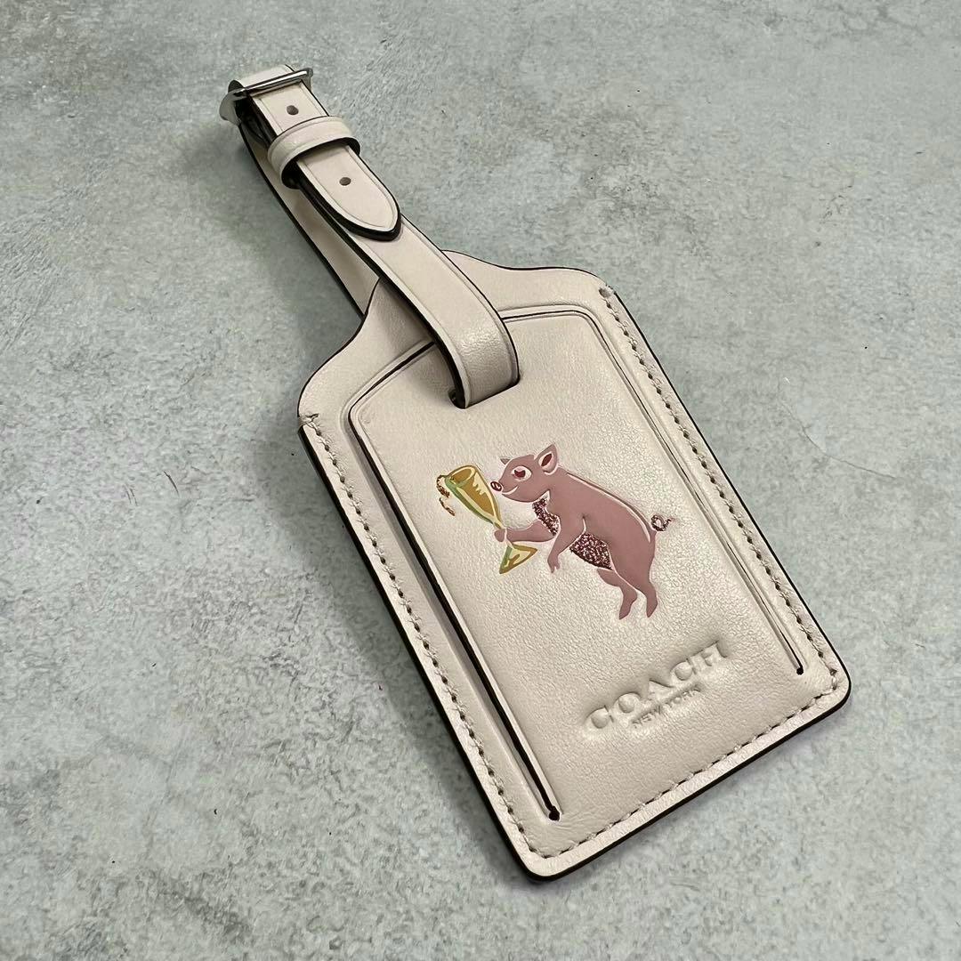 Front of a COACH leather luggage name tag bag charm showing a pig animal motif holding a trophy and the COACH embossed logo.