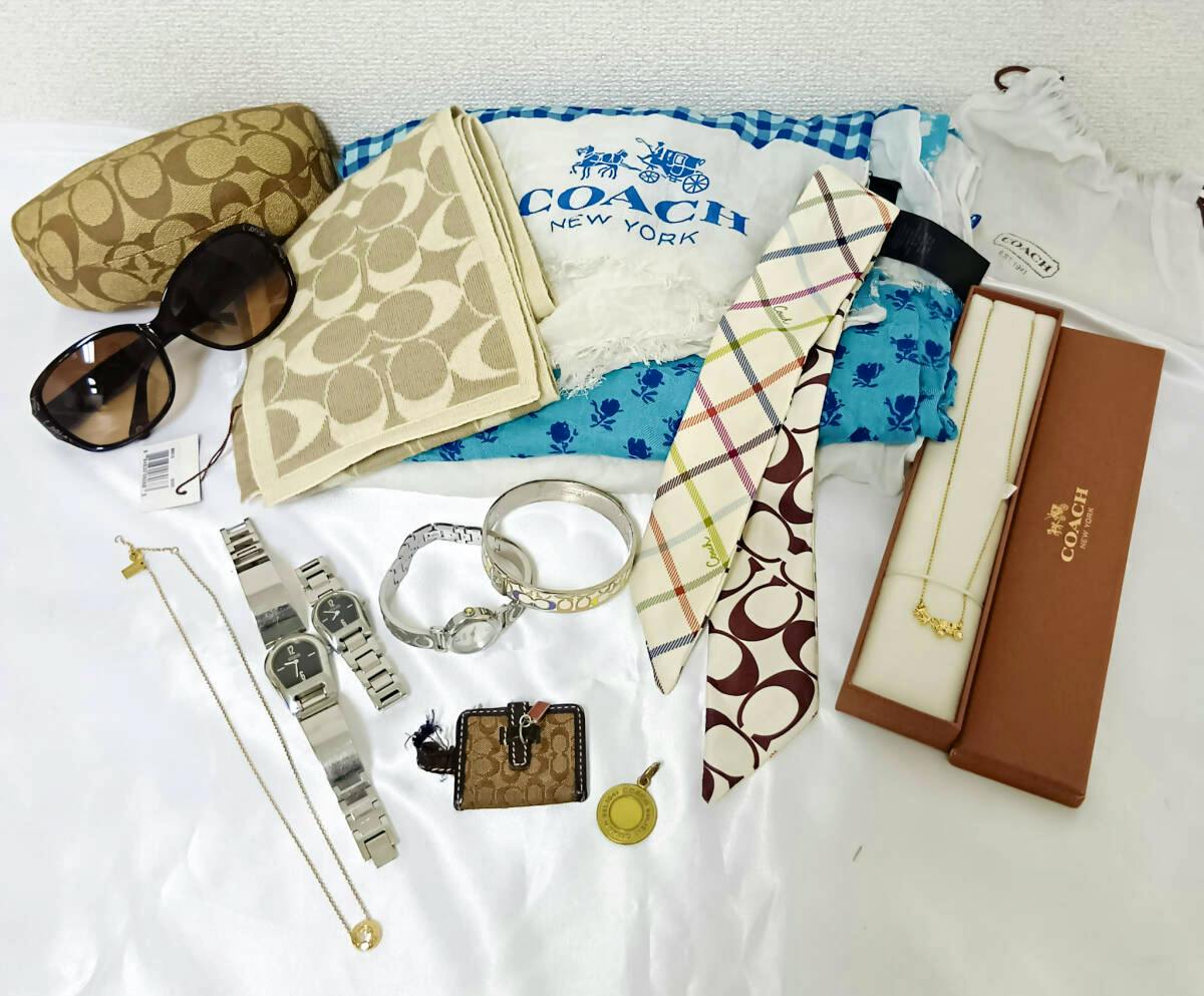Flat lay of multiple Coach accessories including a canvas card holder, scarves, sunglasses, watches, bracelets, and a boxed necklace.