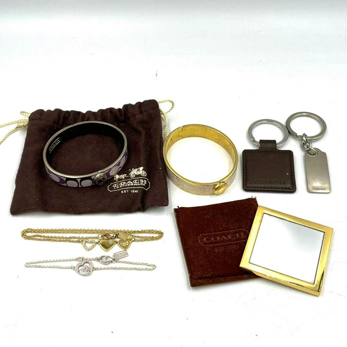 Multiple Coach accessories including bracelets, necklaces, keychains, and a hand mirror arranged on a white background.