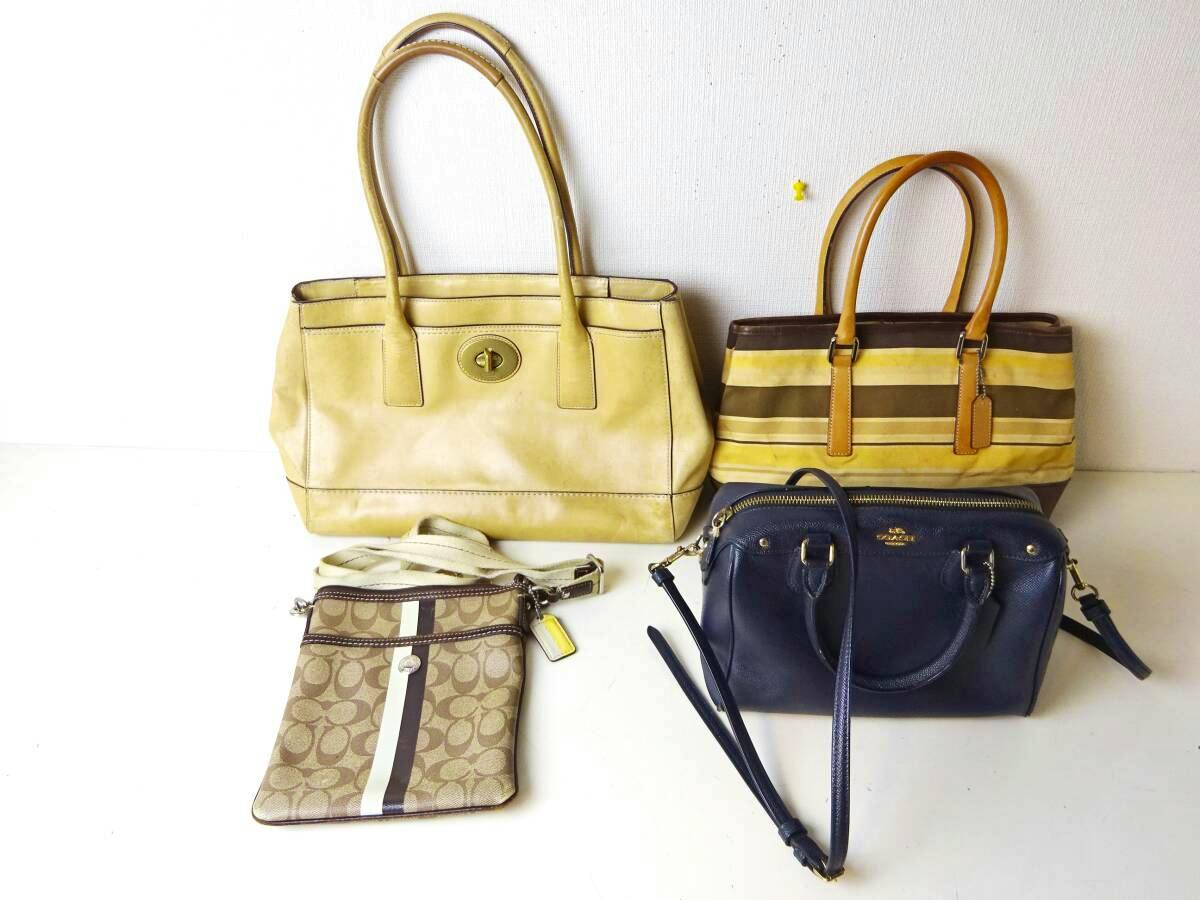 Four COACH bags of assorted styles arranged on a white surface against a white wall.