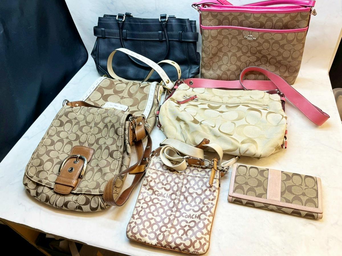 Seven COACH canvas bags and wallets arranged on a table showing signature monogram patterns and straps.