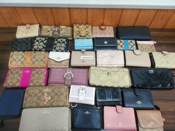 Top-down photo of 30 used Coach wallets and small leather goods arranged on a wooden surface.