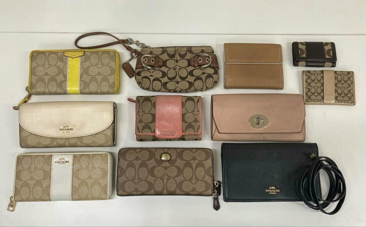 A flat lay of multiple used COACH wallets, card cases, pouches, and a small black bag with strap arranged on a white background.