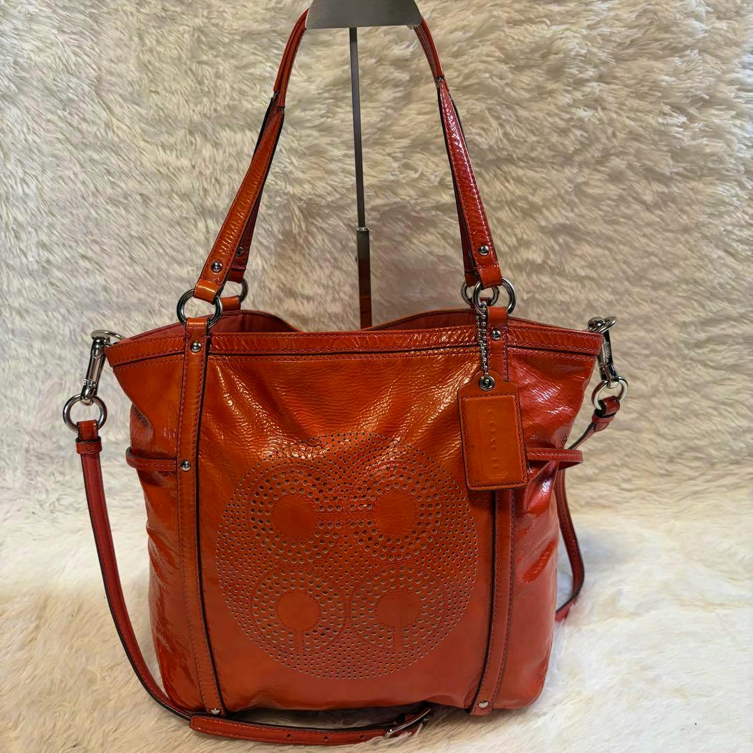 Front view of the COACH Audrey Op Art 2way Bag in orange showing the perforated op art design and straps.