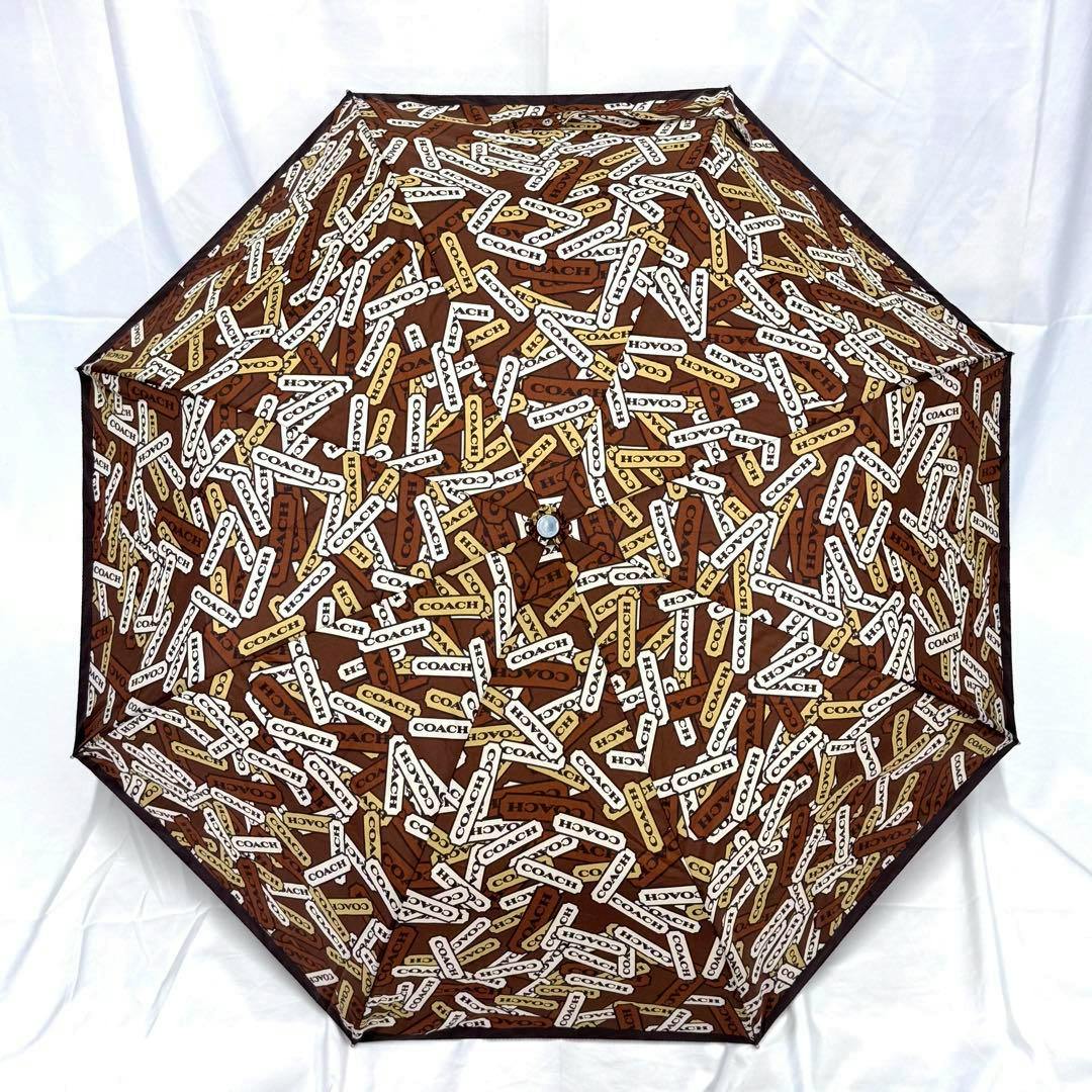 Opened brown COACH folding umbrella showing the all-over COACH logo print on the canopy.