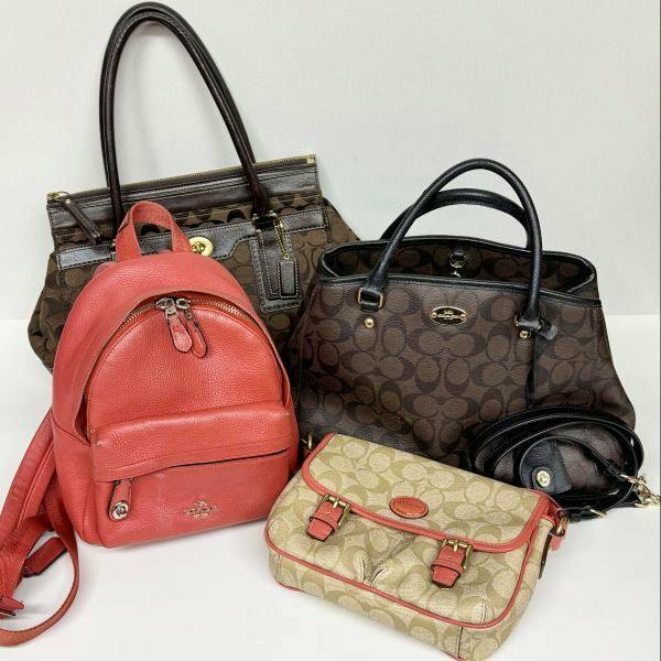 Four Coach bags displayed together on a white surface, including a red leather backpack and three signature-print/black-handle bags.