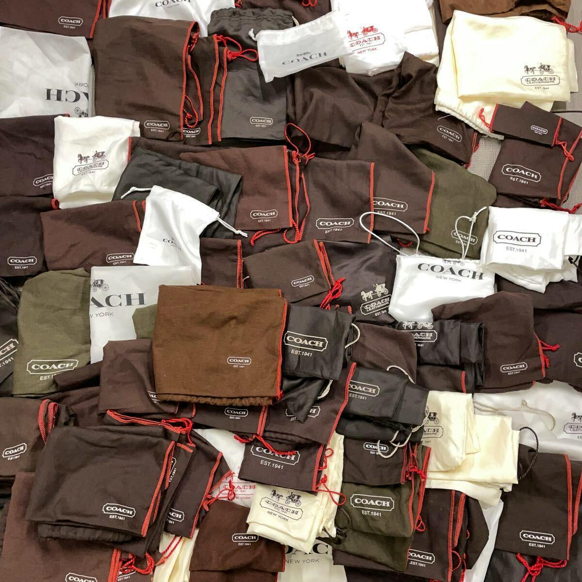 A large assortment of COACH-branded drawstring dust bags and small pouches in brown, white, and cream piled together.