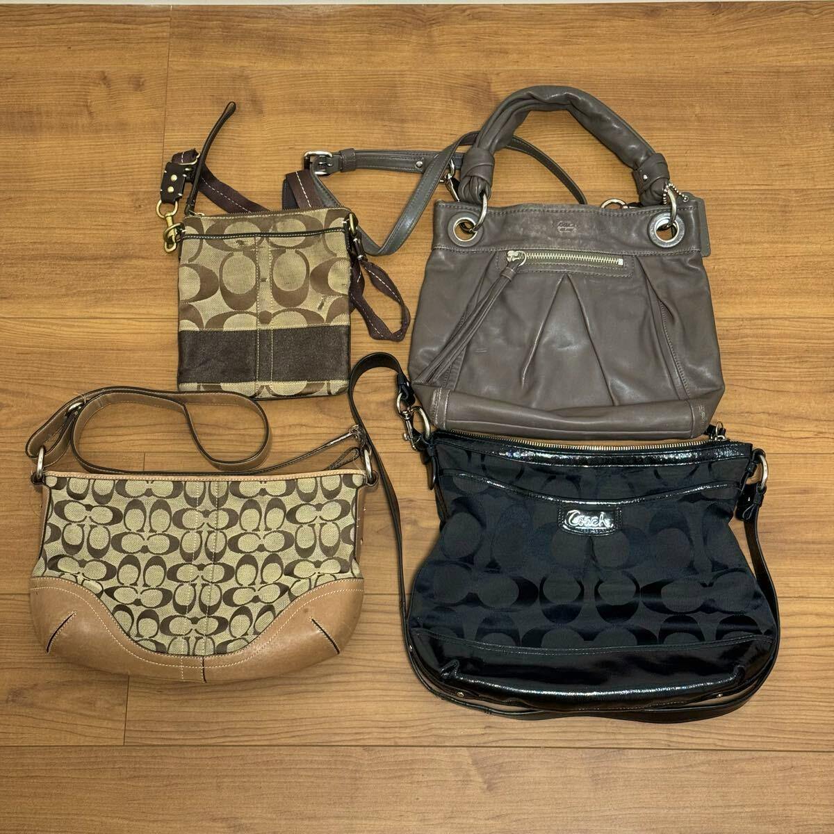 Four Coach bags including signature canvas and leather styles arranged on a wooden floor.