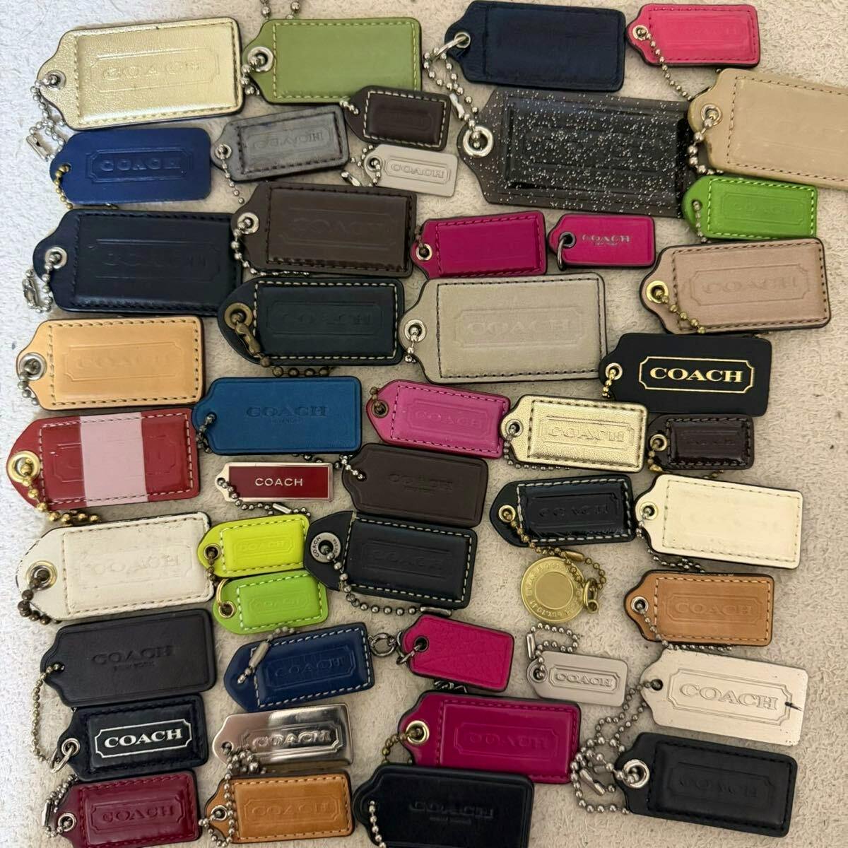 A large assortment of COACH leather bag charm name tags and keychain charms in various colors laid out on a surface.