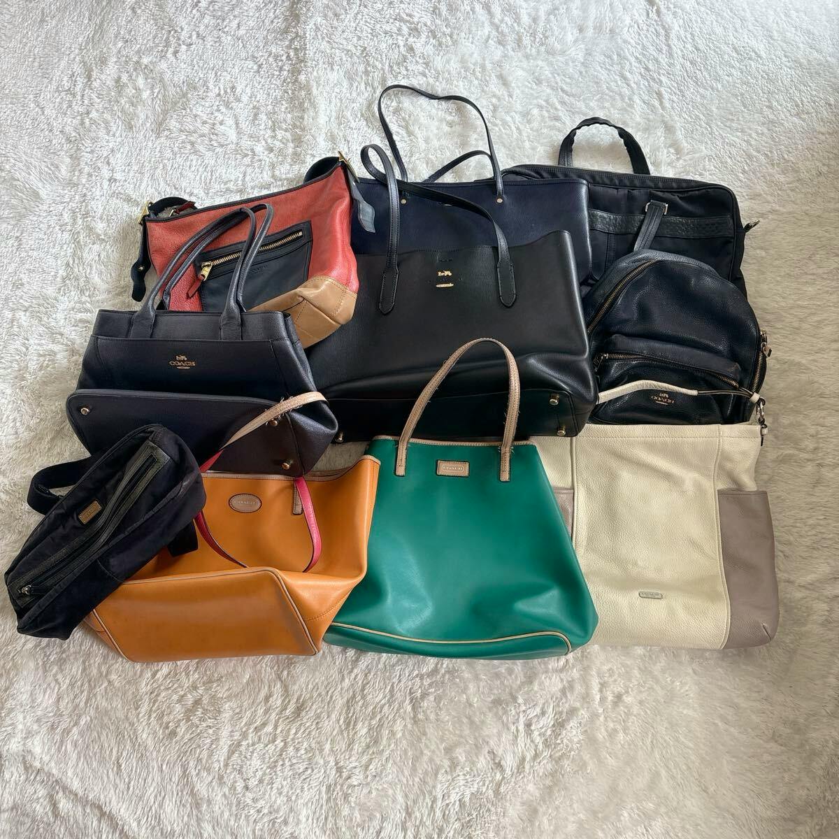 A collection of COACH bags and totes in various colors arranged on a light rug.