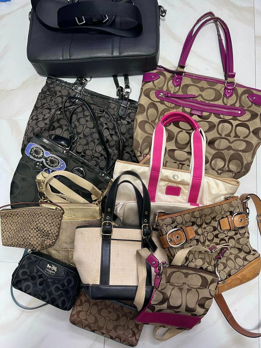Multiple Coach shoulder and tote bags in various signature monogram patterns and colors arranged on a white floor.