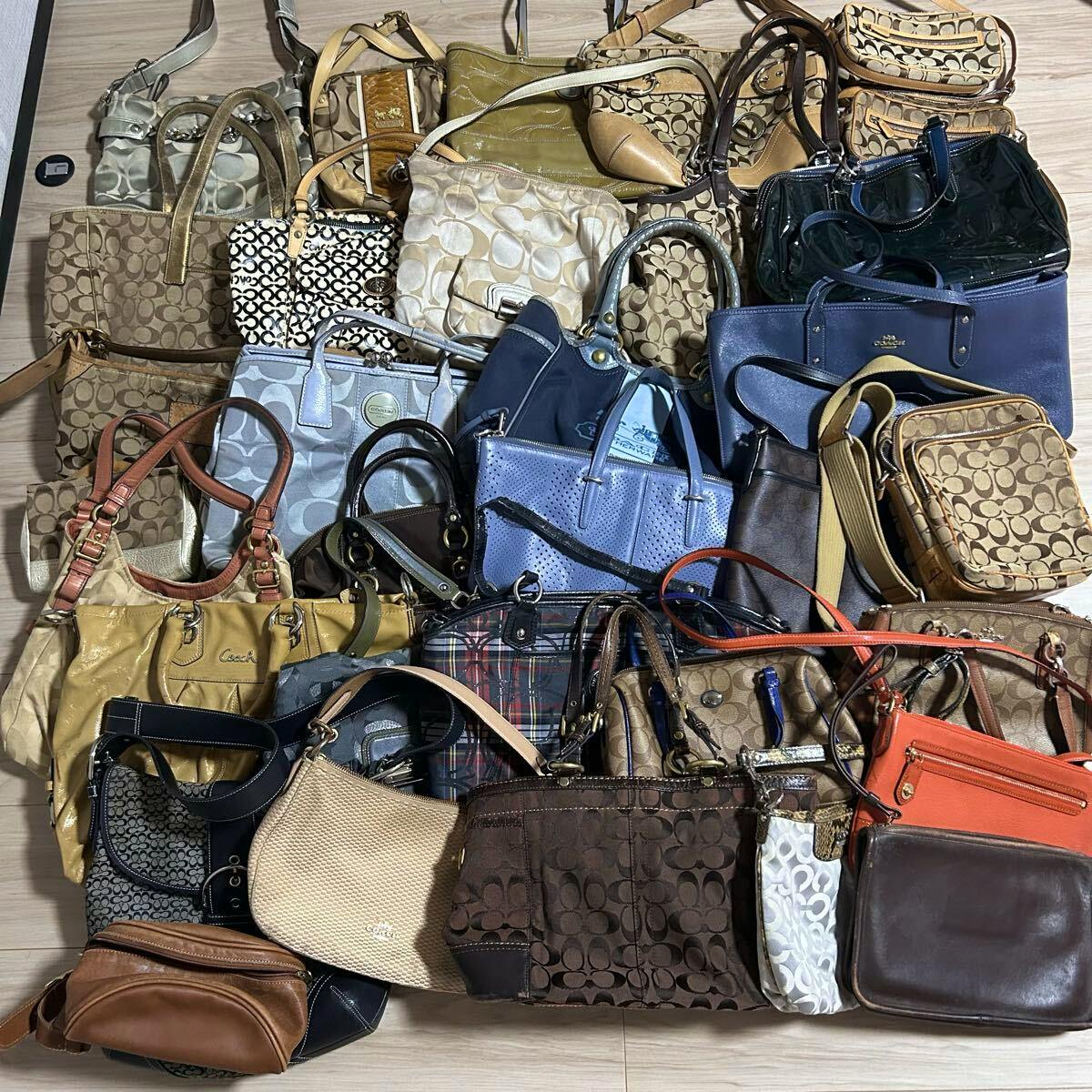 A spread of assorted COACH handbags, totes, and shoulder bags arranged on a floor showing various canvas and leather styles.