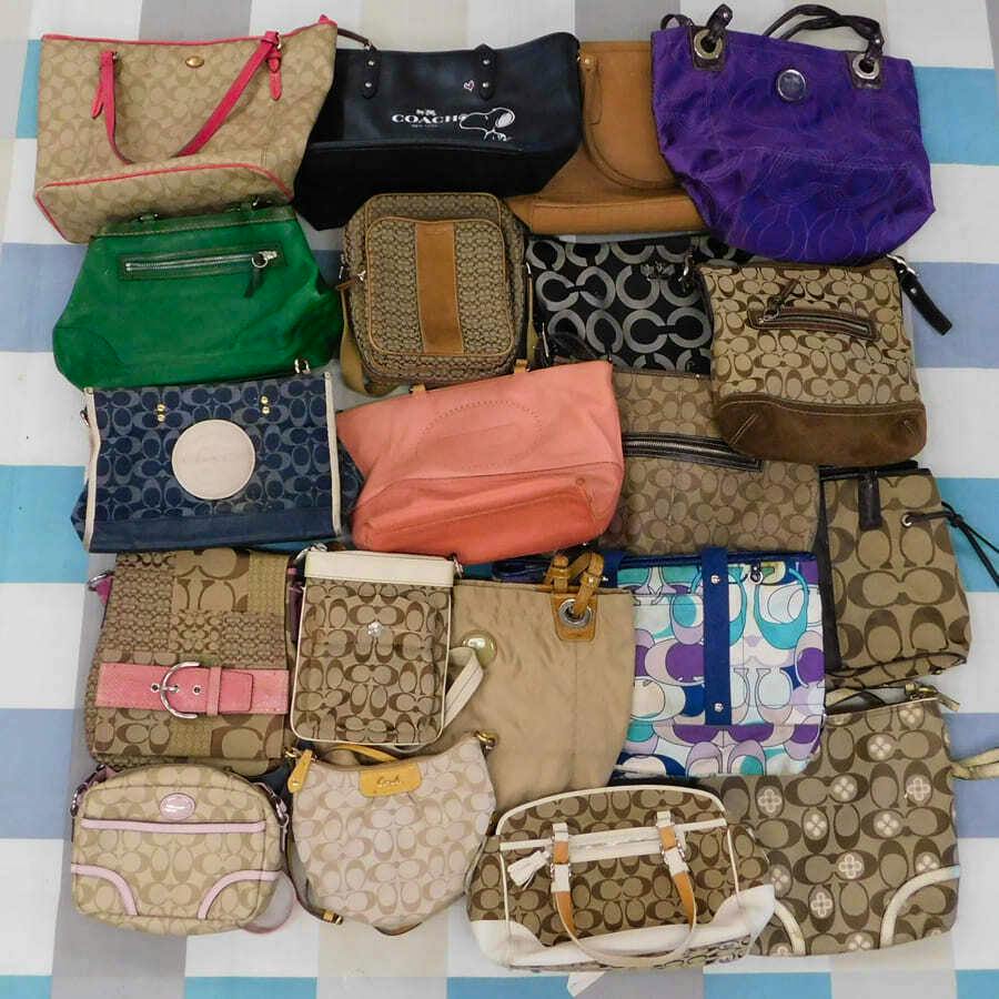 A collection of about twenty Coach bags in various colors and signature patterns arranged on a striped surface.