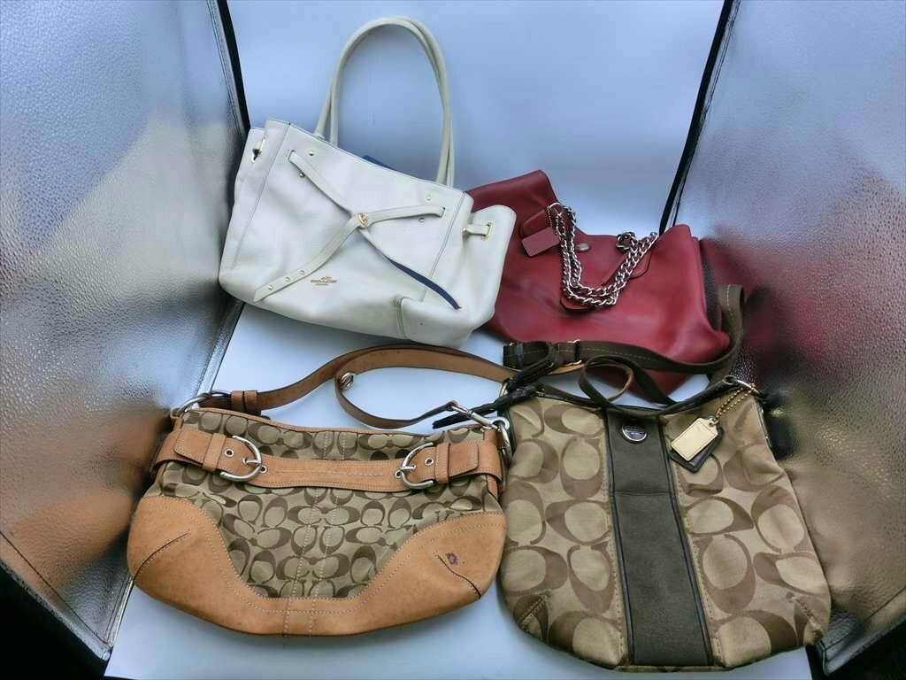 Four Coach bags in different styles and colors displayed together on a reflective background.