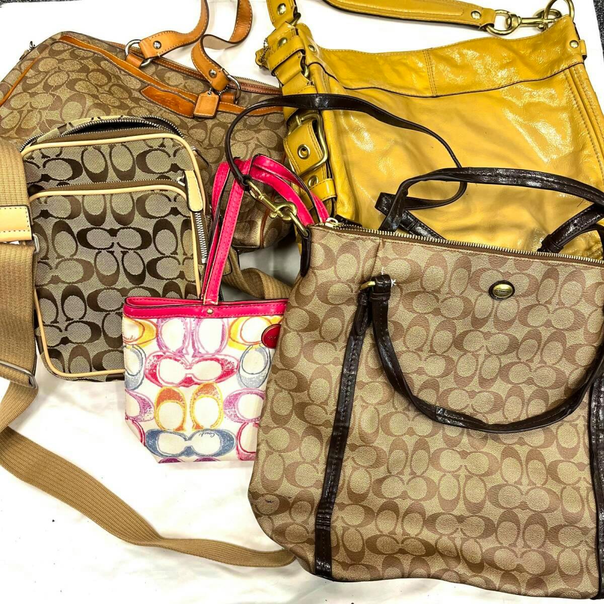 Several Coach bags laid out together, showing multiple brown signature monogram canvas bags, a yellow bag, and a small multicolored bag.