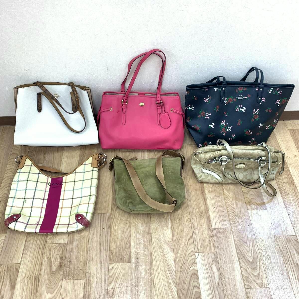 Six Coach bags in various colors and styles arranged on a wooden floor against a light-colored wall.