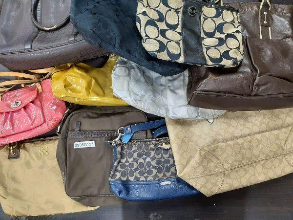 Multiple used Coach bags and pouches in various colors arranged overlapping on a surface.