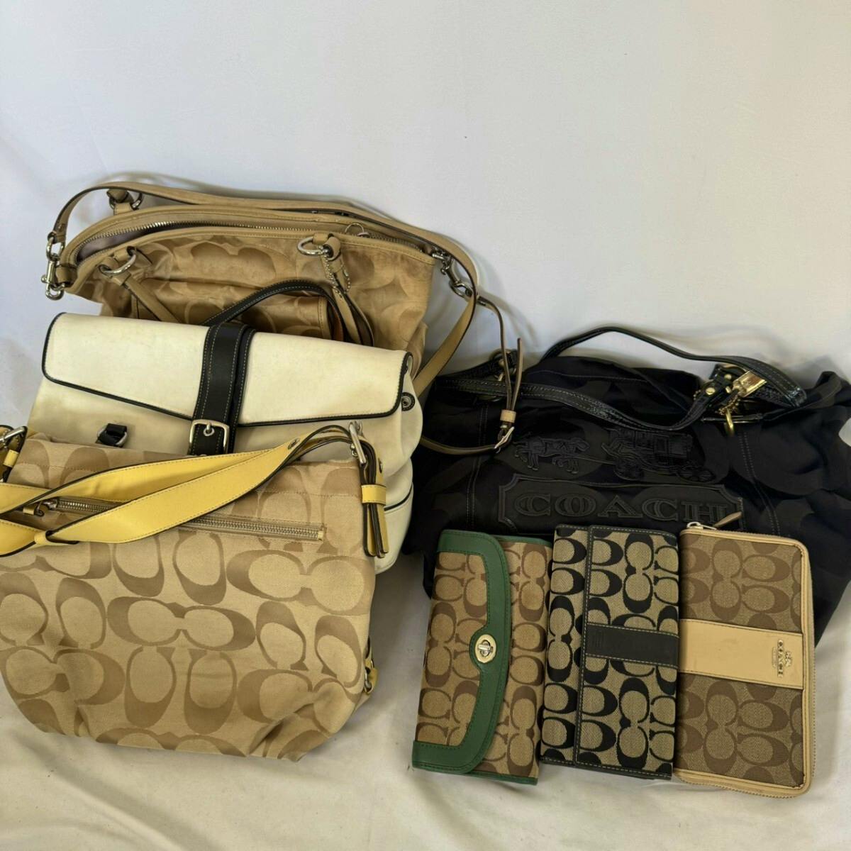 Multiple COACH bags and wallets from a bulk set arranged on a white background, showing signature C canvas patterns and leather trim.