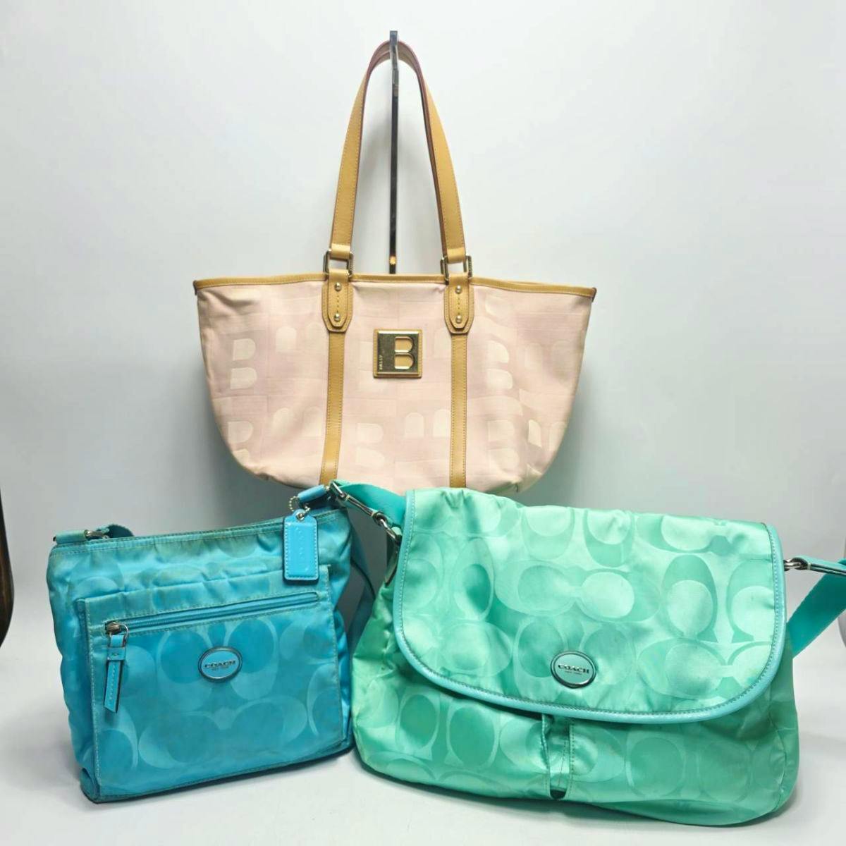 Three-piece set of brand bags: a beige tote with a gold B emblem and two turquoise Coach shoulder bags on a white background.
