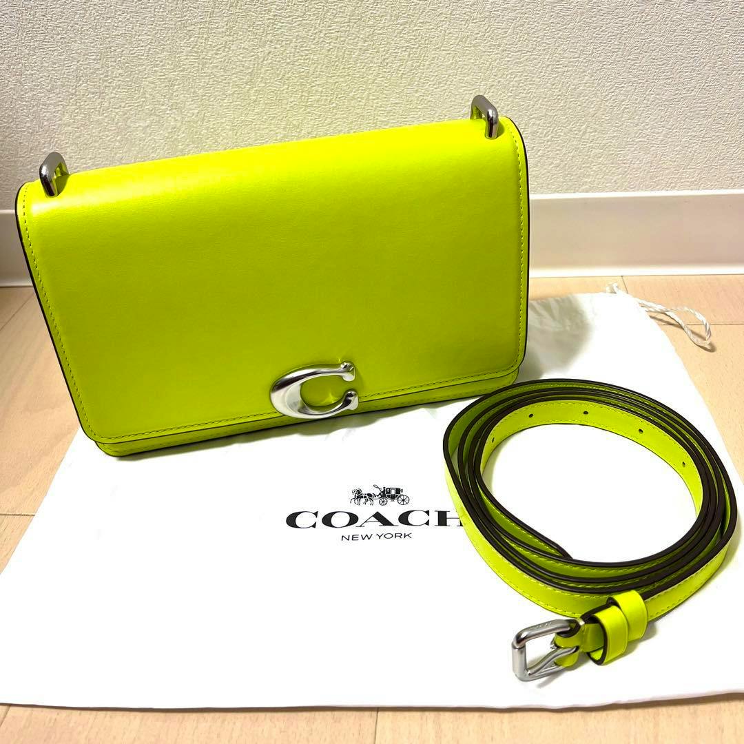 Neon yellow Coach Bandit shoulder bag with a matching detachable strap placed on a Coach dust bag.
