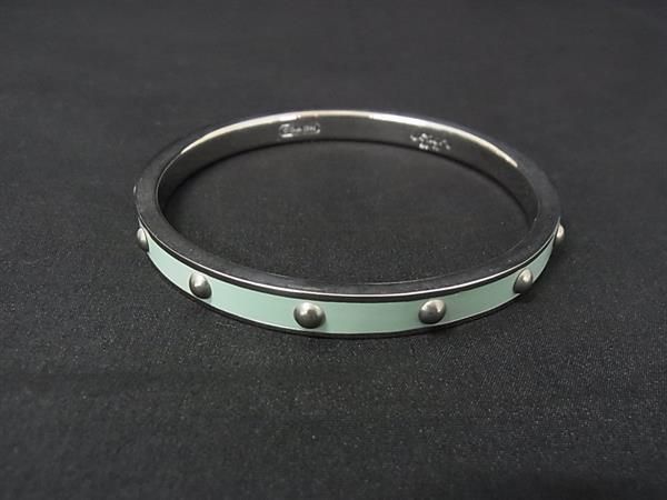 A Coach mint-green enamel and silver-tone bangle bracelet with round studs on a black background.