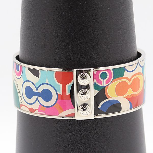 Colorful Coach bangle bracelet with multicolored enamel pattern and metal clasp shown on a black display stand.