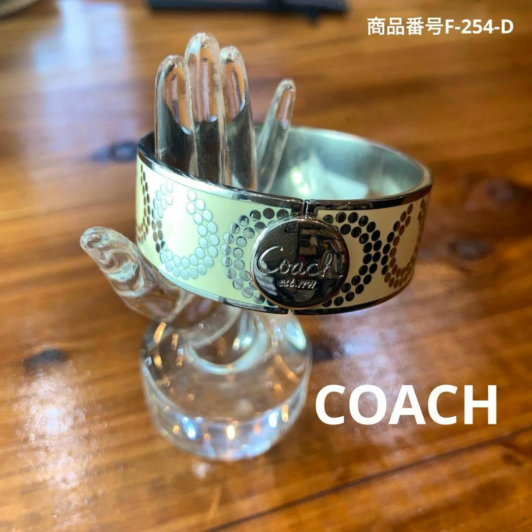 Coach bangle bracelet with cream-colored enamel and circular dot pattern displayed on a clear hand stand.