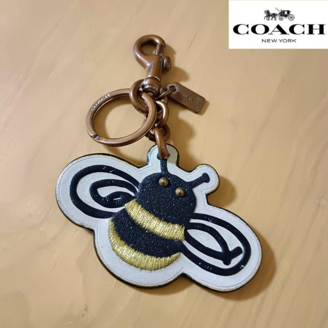 Front view of a COACH bee-motif leather keychain charm with metal ring and clasp.