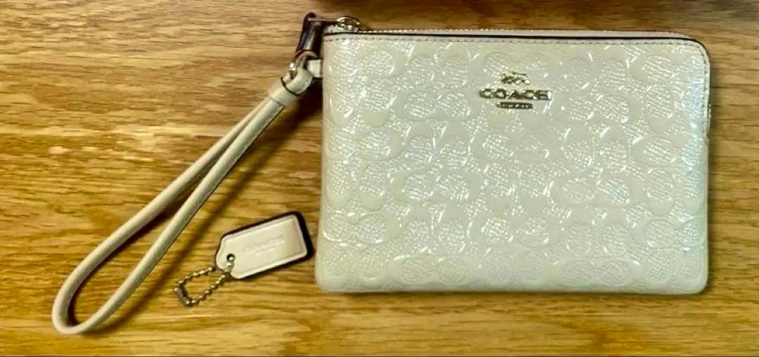 Beige COACH leather wristlet pouch with strap and small tag on a wooden surface.