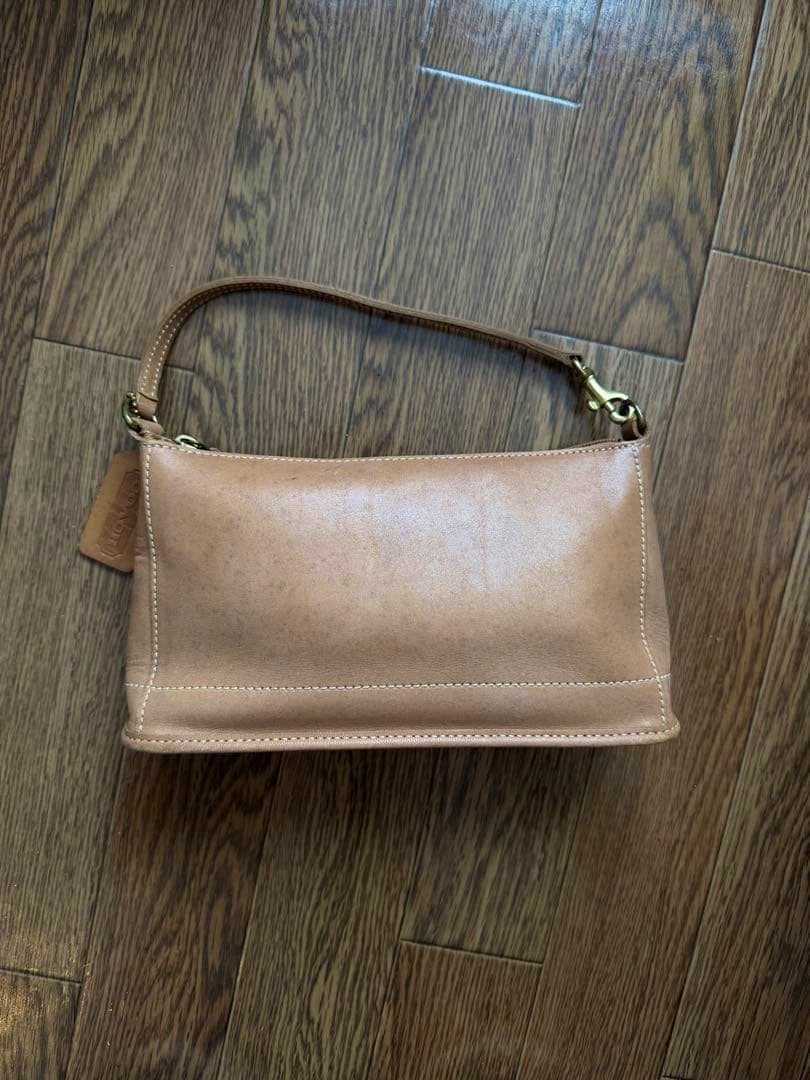 Beige Coach leather pouch with short strap placed on a wooden floor.