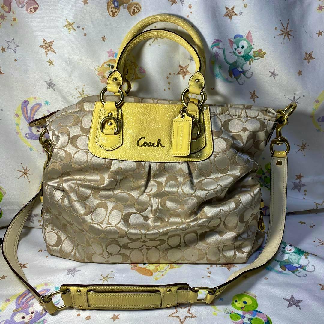 Beige Coach shoulder bag (cow leather) with yellow leather trim and a detachable shoulder strap shown front-facing on patterned fabric.