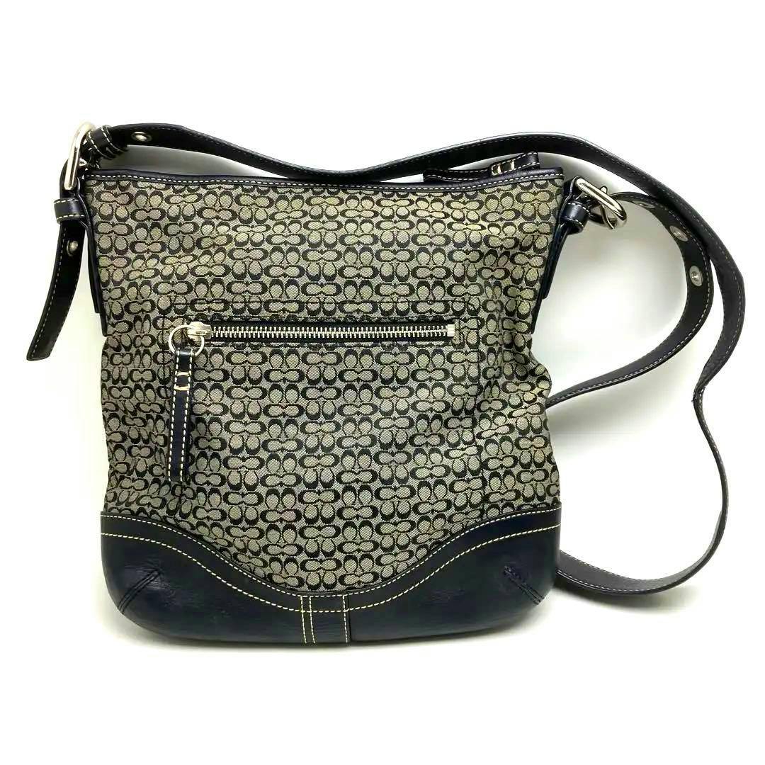 Front view of a Coach shoulder bag in black and gray patterned canvas with a front zipper pocket and dark leather trim.