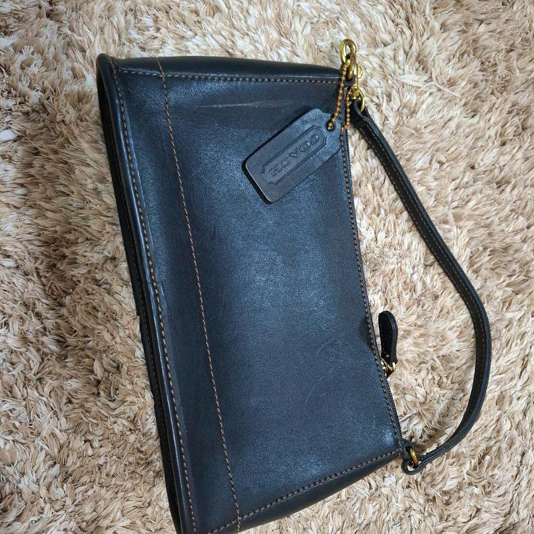 Black Coach leather pouch with a wrist strap and Coach tag photographed flat on a shag rug.