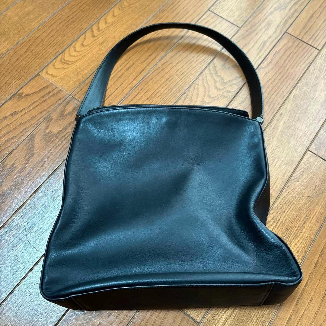 Black cow leather COACH hand bag with a single shoulder strap lying on a wooden floor.