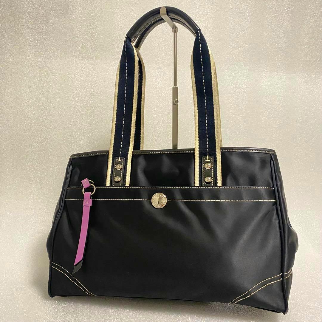 Front view of a black Coach nylon shoulder bag with two striped handles, a gold-tone logo medallion, and a pink leather strap detail.