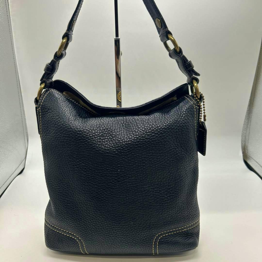 Front view of a black pebbled leather COACH shoulder bag with a short leather strap and brass hardware.