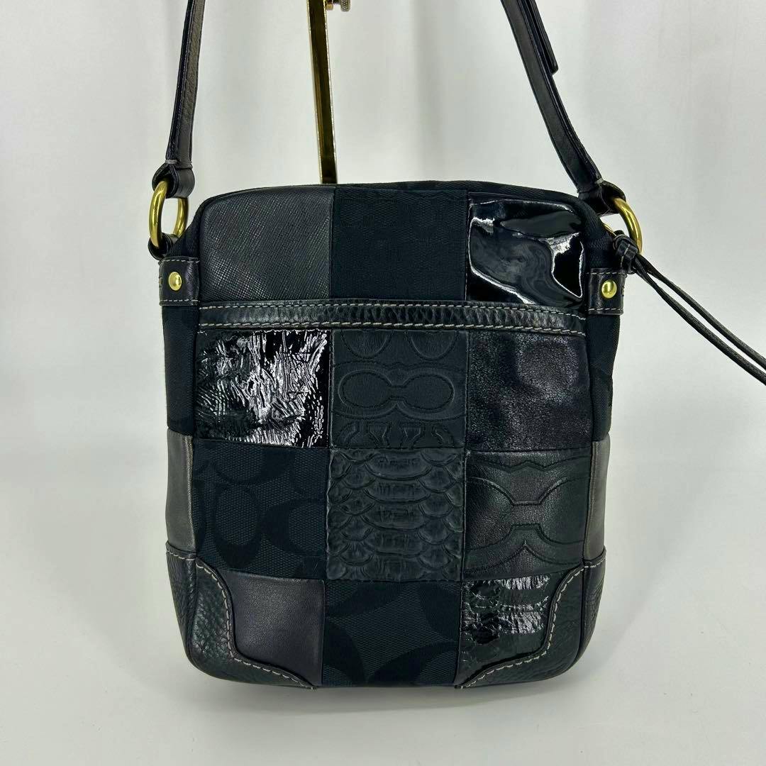 Front view of a black Coach patchwork shoulder bag with mixed leather and fabric panels, stitched corners, a long shoulder strap, and gold-tone hardware.