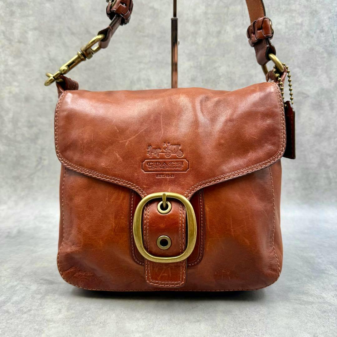 Brown Coach Bleecker cow leather shoulder bag with front flap, embossed logo, and brass buckle.