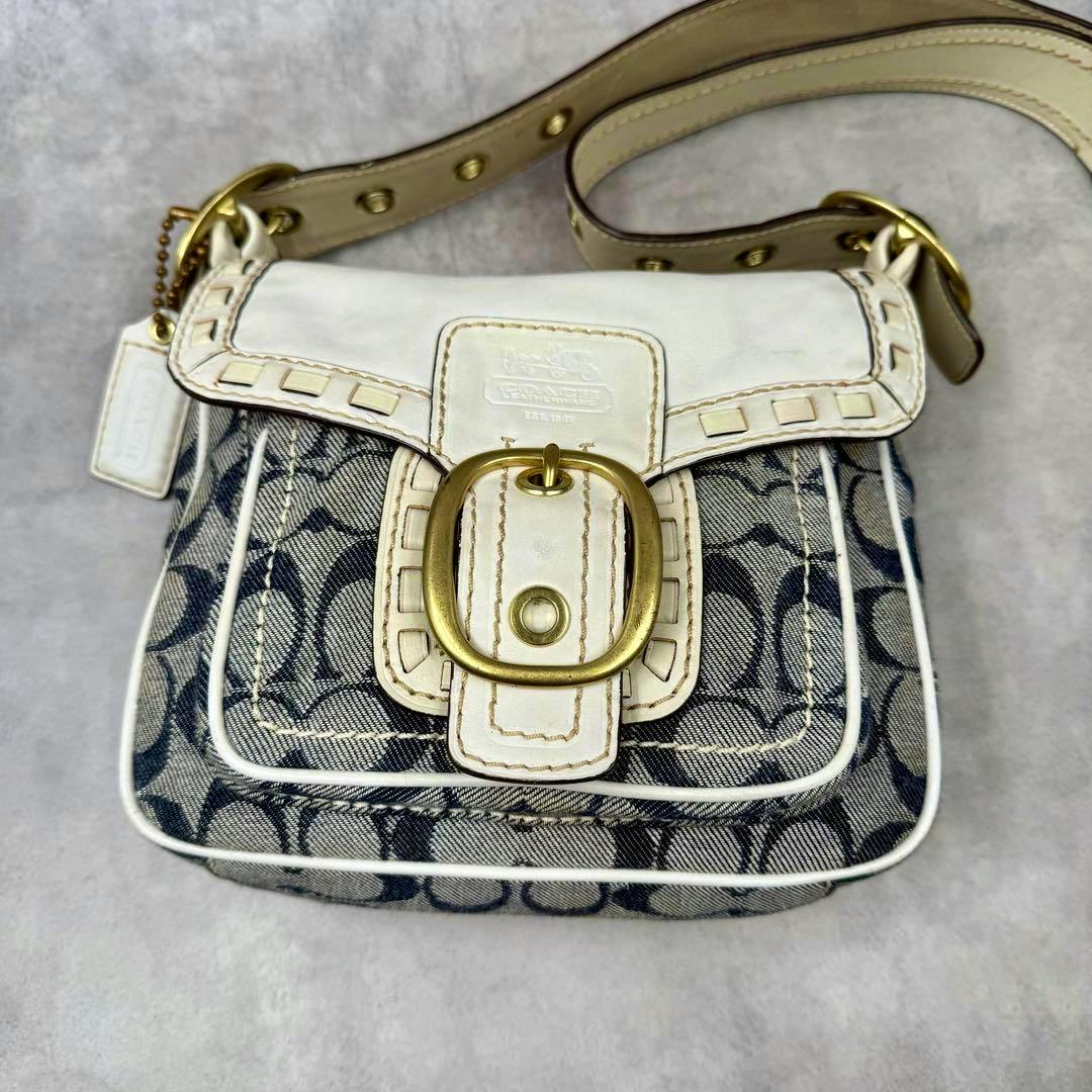Front view of the COACH ブリーカー shoulder bag in denim signature canvas with white leather trim and a brass buckle.