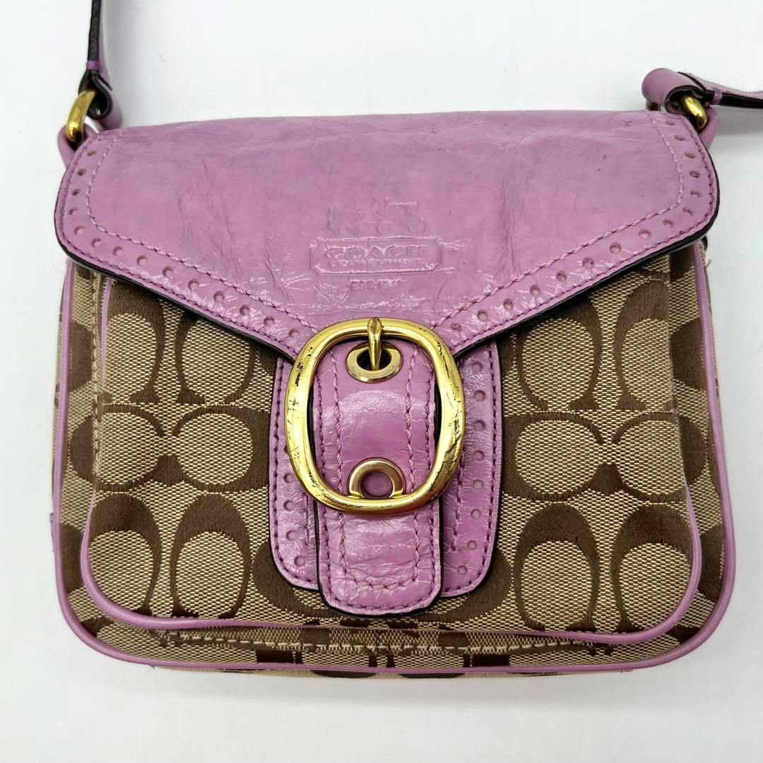 Front view of a Coach signature canvas shoulder bag with a purple leather flap and gold buckle.