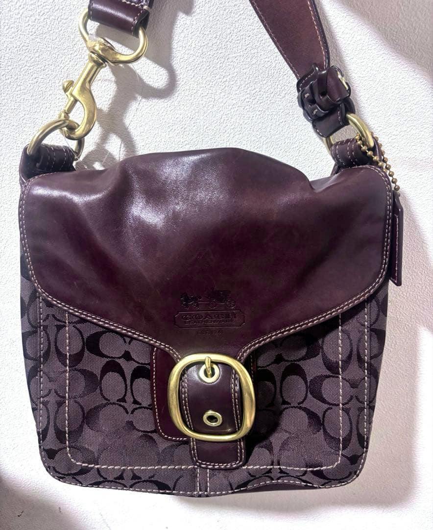 Front view of the COACH SOHO one-shoulder cow leather bag with signature fabric body, leather flap, and brass buckle.