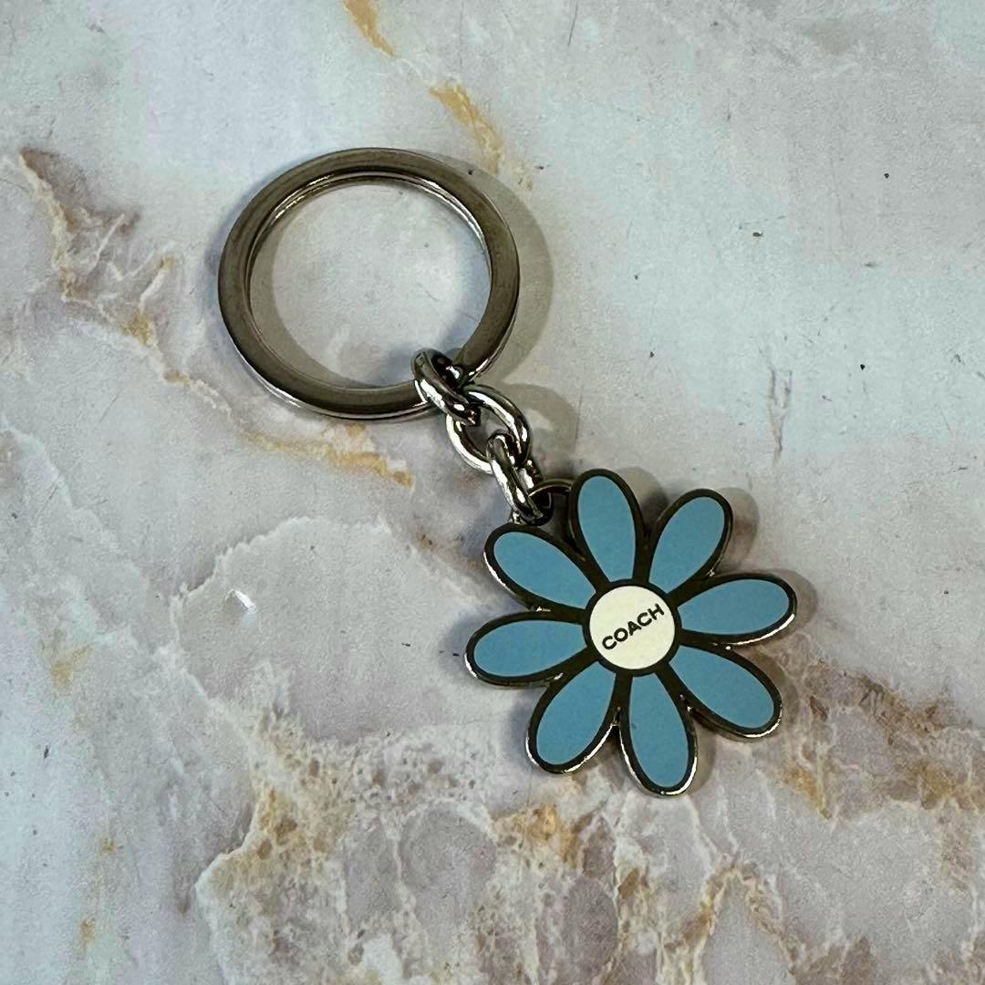 Blue flower-shaped metal bag charm key ring showing "COACH" in the center, attached to a silver key ring.