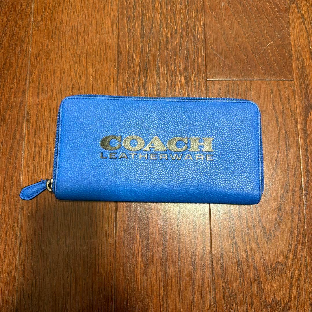 Blue COACH cow leather long zip-around wallet showing the COACH LEATHERWARE logo on a wooden surface.