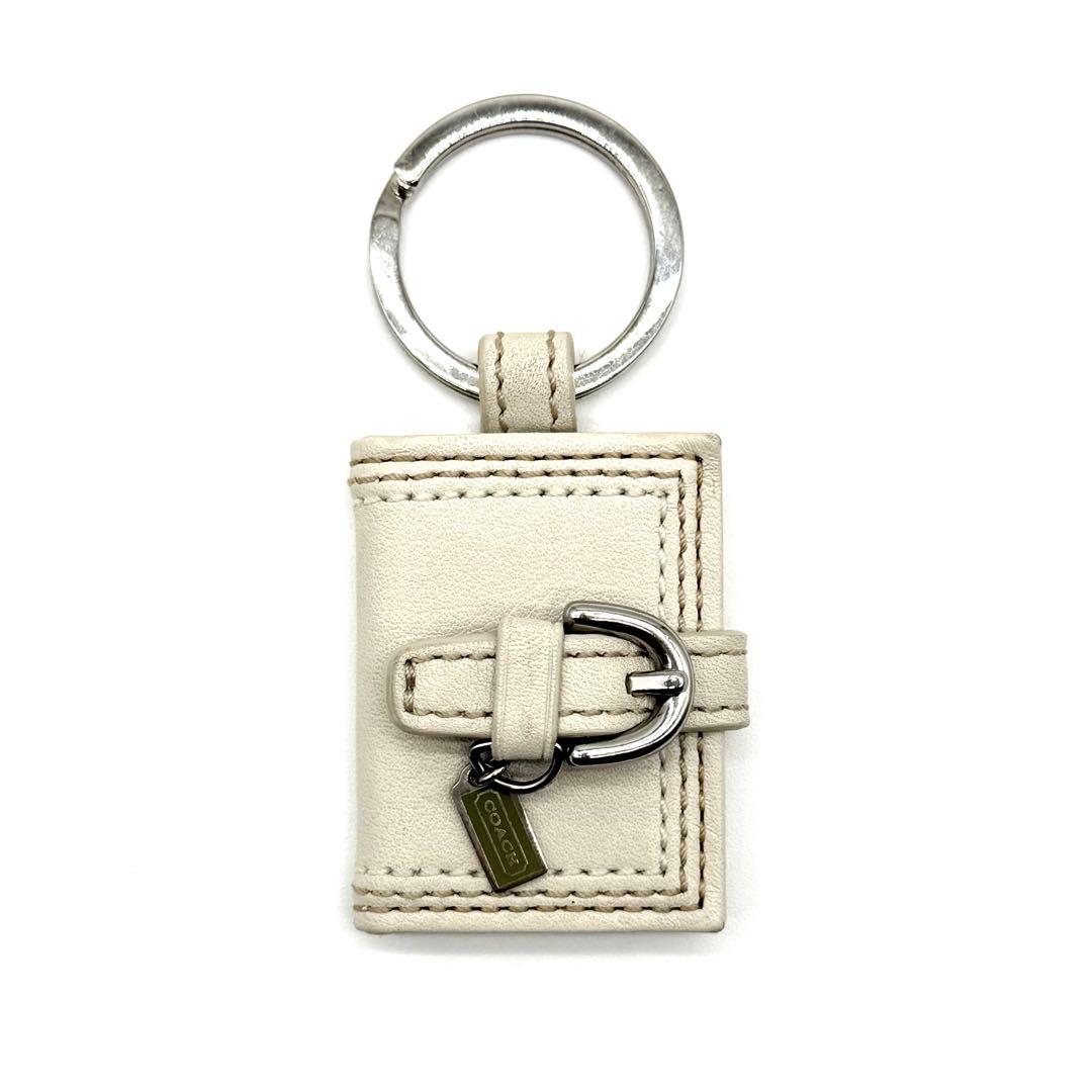 White Coach book-style leather keychain with a metal ring, buckle, and small tag.