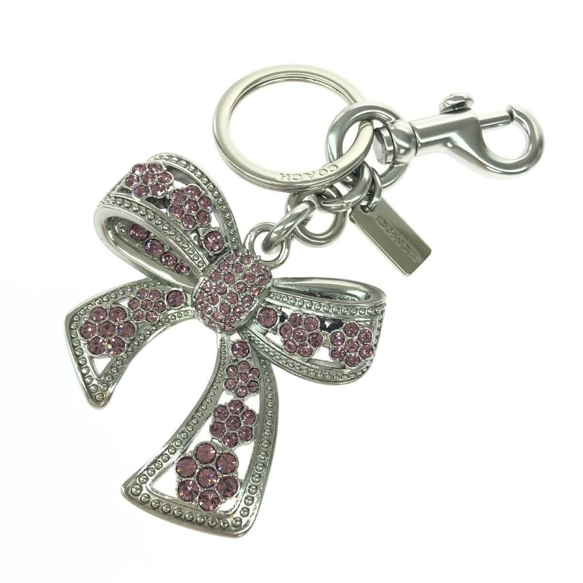 COACH bow bag charm/keyring in silver color with pink crystal embellishments attached to a key ring and clasp.